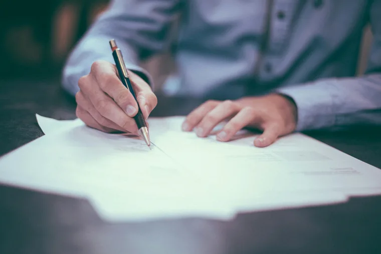 Person signing loan agreement documents at desk, illustrating the Crane Finance loan review and signing process